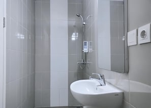 Une salle de bain moderne avec un lavabo blanc, une douchette à main et un miroir fixé au mur.