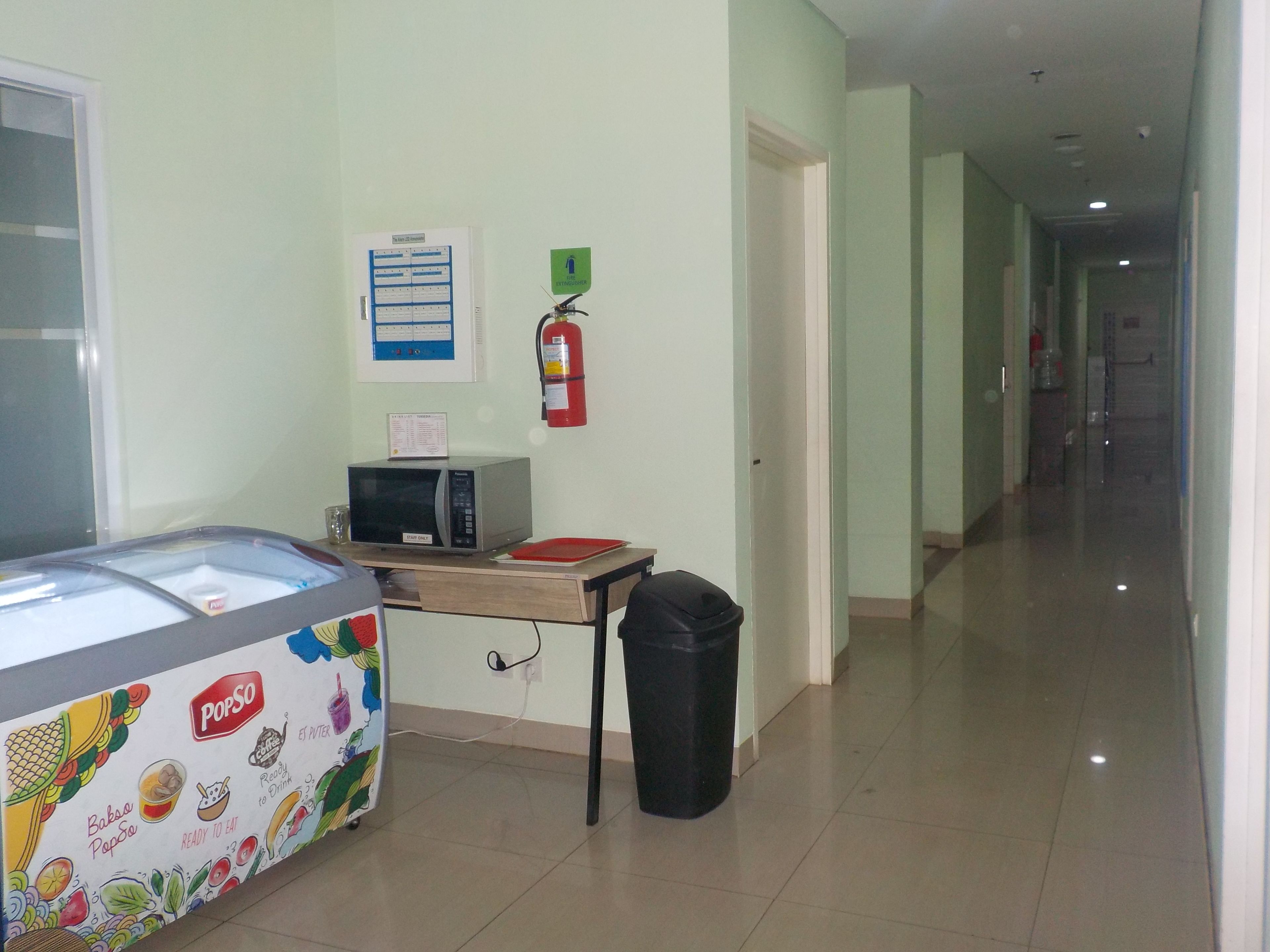 A corridor with a microwave on a table, a fire extinguisher, and a trash bin.