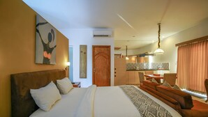 A hotel room with a large bed, a wooden headboard, a dining area with a table and chairs, and a kitchen in the background. - Ocean View Residence - Hotel Jepara (Jepara)