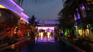 A nighttime view of a hotel pool area with palm trees and a building with illuminated windows. - Ocean View Residence - Hotel Jepara (Jepara)