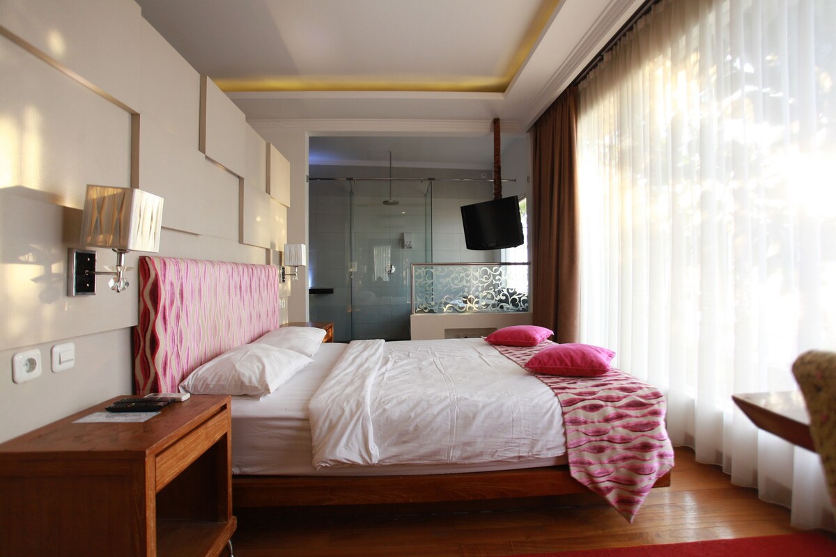 A bedroom with a bed, bedside table, lamp, and a view of a bathroom.