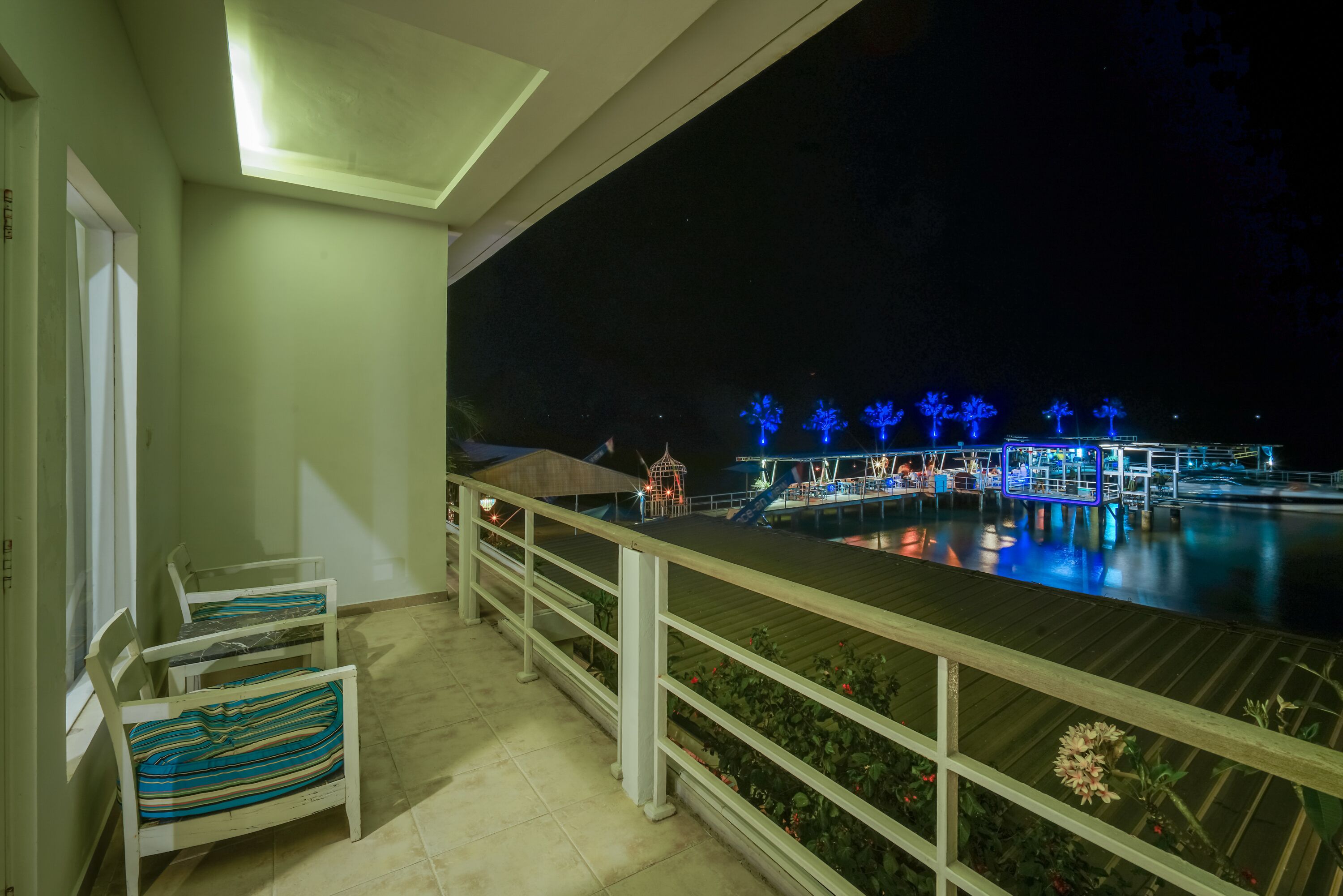 Un balcon donnant sur une piscine la nuit, avec des arbres illuminés et une fontaine.