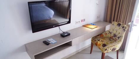 A flat-screen TV mounted on a wall, a remote control, a power strip, and a patterned chair.