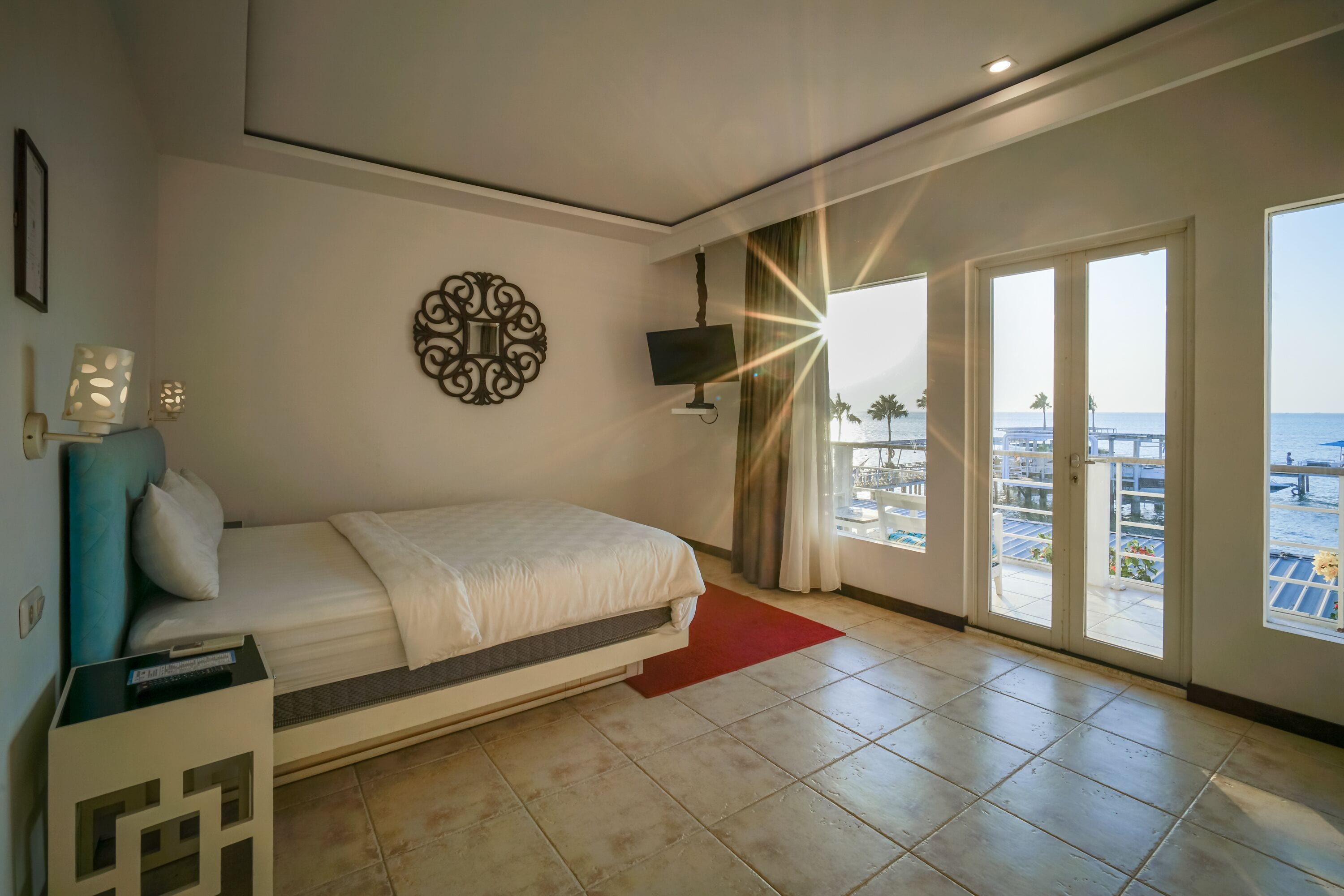 Una camera da letto con un letto, una TV, un elemento decorativo al muro e vista mare attraverso ampie finestre.