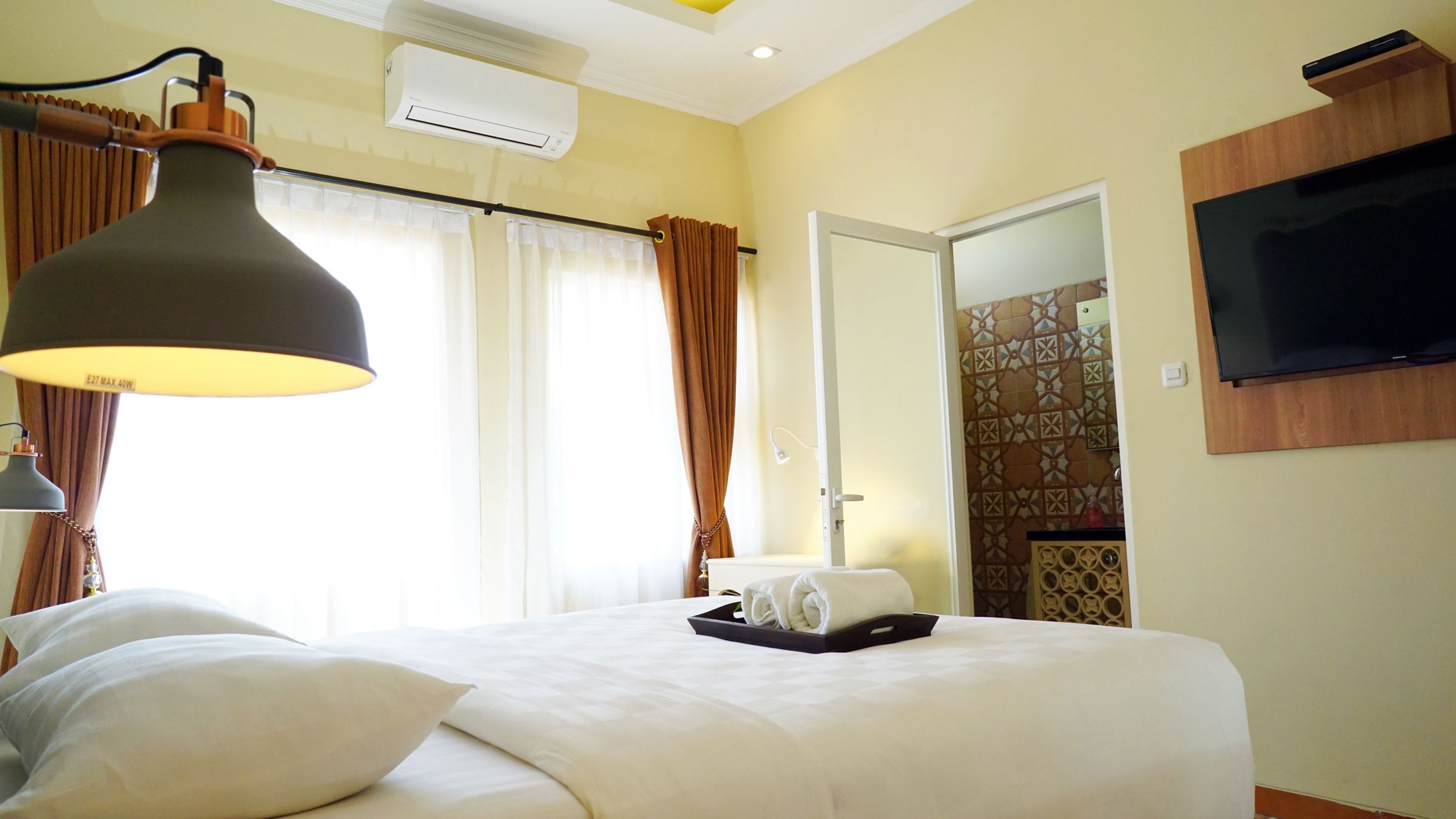 Ein Hotelzimmer mit Bett, Flachbildfernseher an der Wand, Klimaanlage und einem fenster mit Vorhängen.