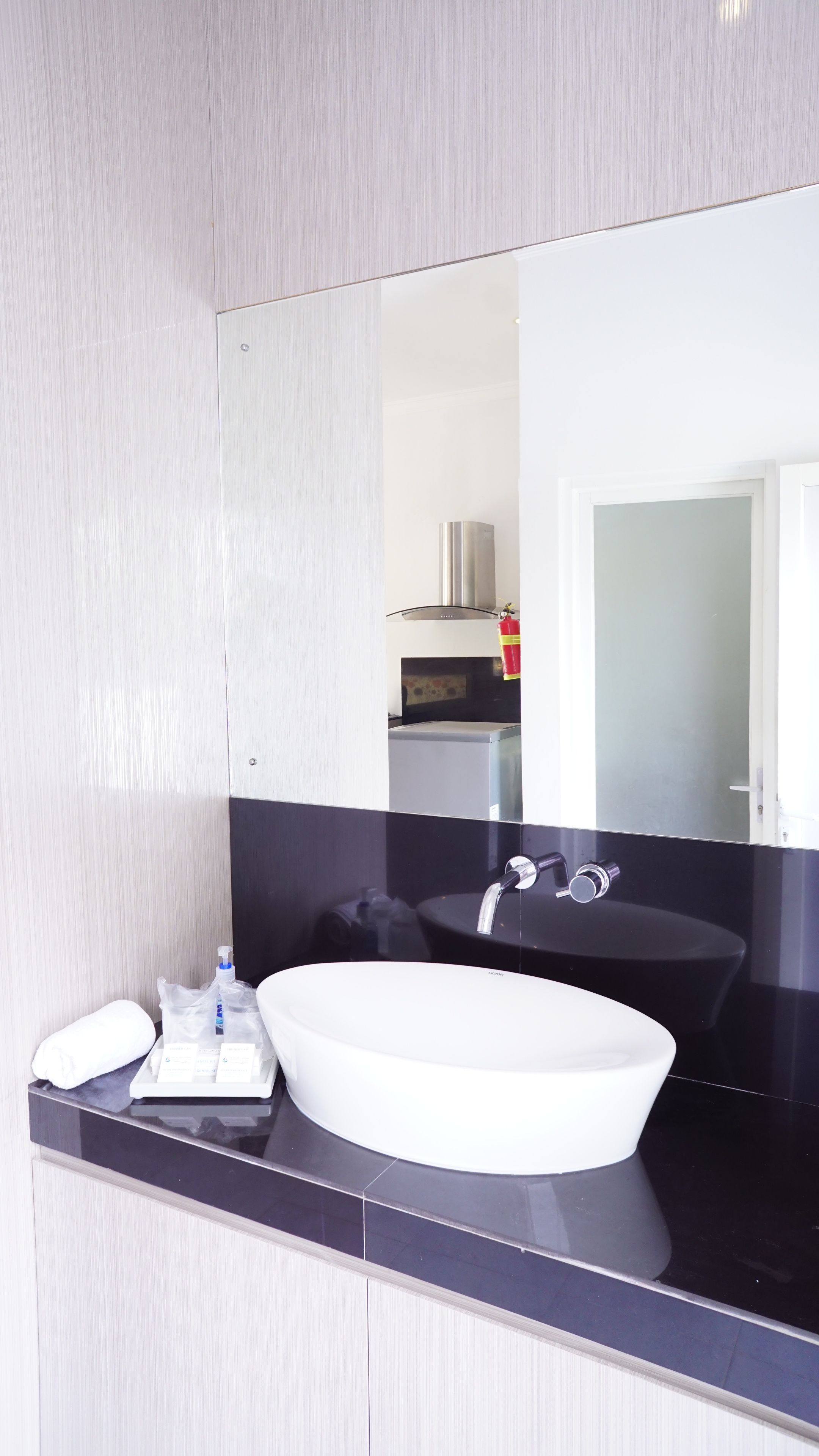 Un bagno moderno con un ampio specchio, un lavandino bianco e un piano d'appoggio nero.