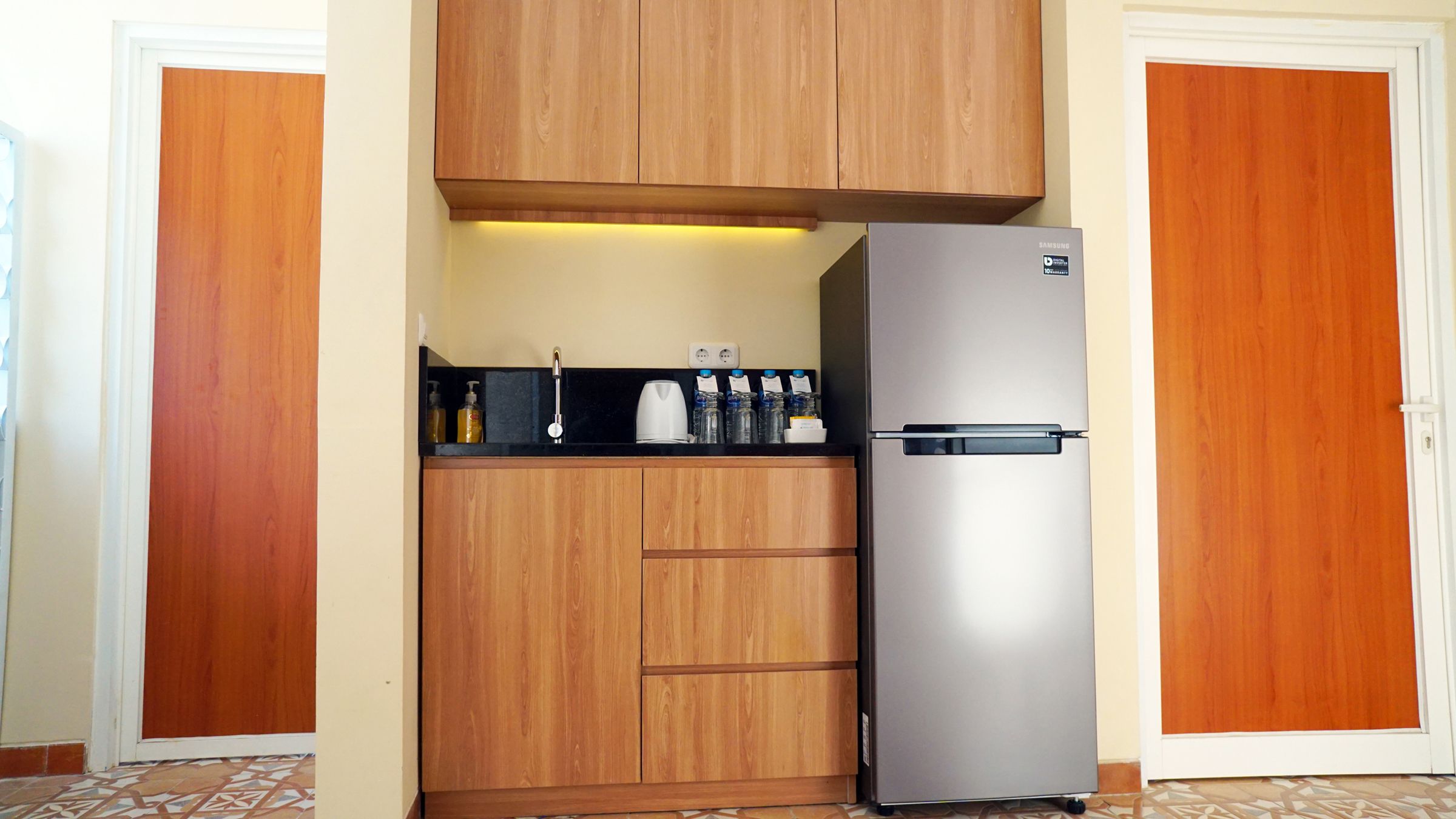 Eine kleine Küche mit Holdekor-Schränken, einem Edelstahl-Kühlschrank und einer schwarzen Arbeitsplatte.