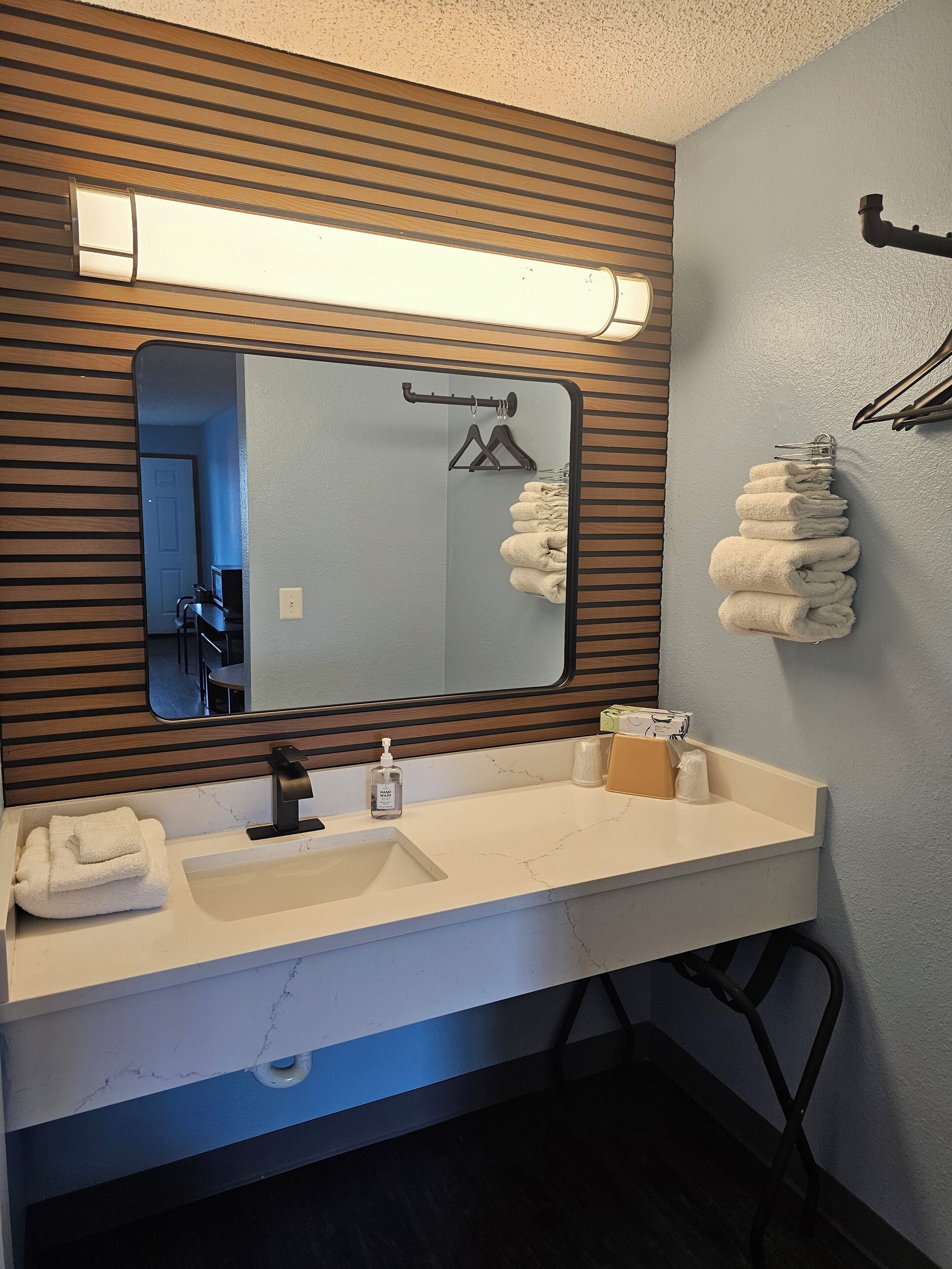 Une salle de bain avec un mur recouvert de panneaux en bois, un grand miroir, un lavabo avec un robinet et un porte-serviettes avec des serviettes pliées.
