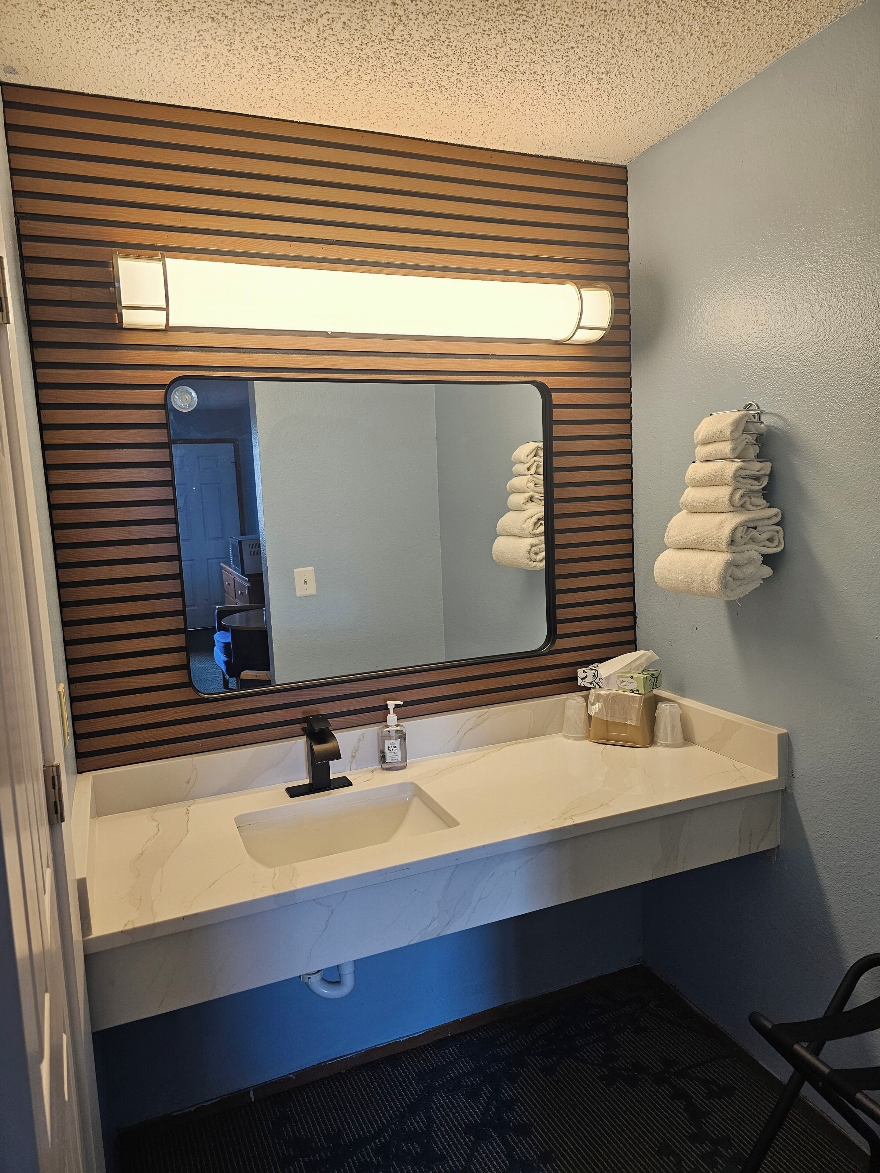 Un baño con un lavamanos blanco, un espejo con paneles de madera y un perchero con toallas.