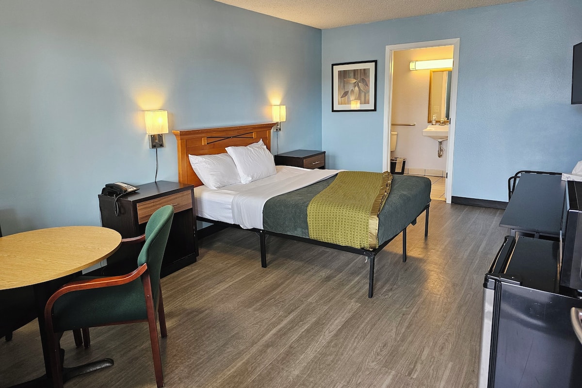 Une chambre d’hôtel comprenant un lit, une table de chevet, un bureau, une chaise et une petite kitchenette.
