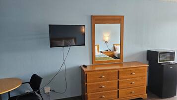 Une chambre d’hôtel équipée d’un téléviseur fixé au mur, d’une commode en bois, d’un four à micro-ondes, d’une chaise et d’une petite table.