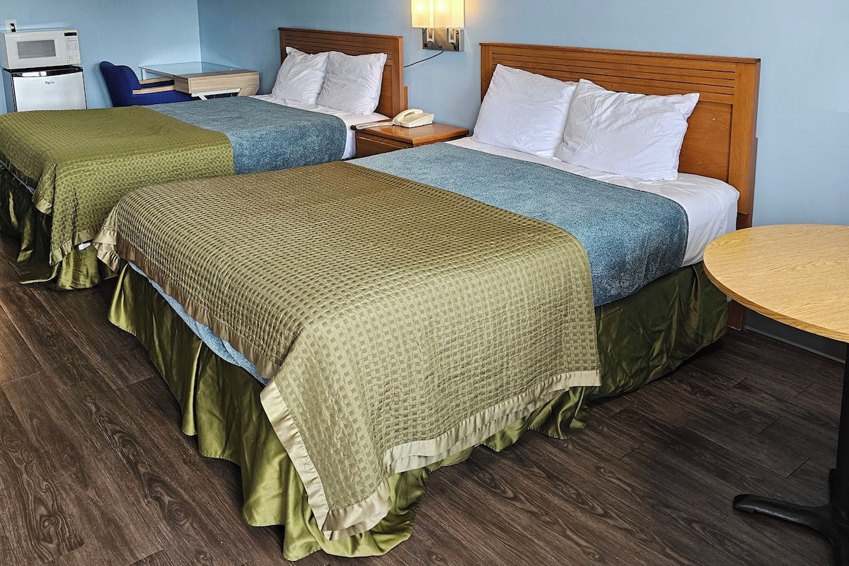 Une chambre d’hôtel avec deux lits, un four à micro-ondes, une petite table et une lampe fixée au mur.