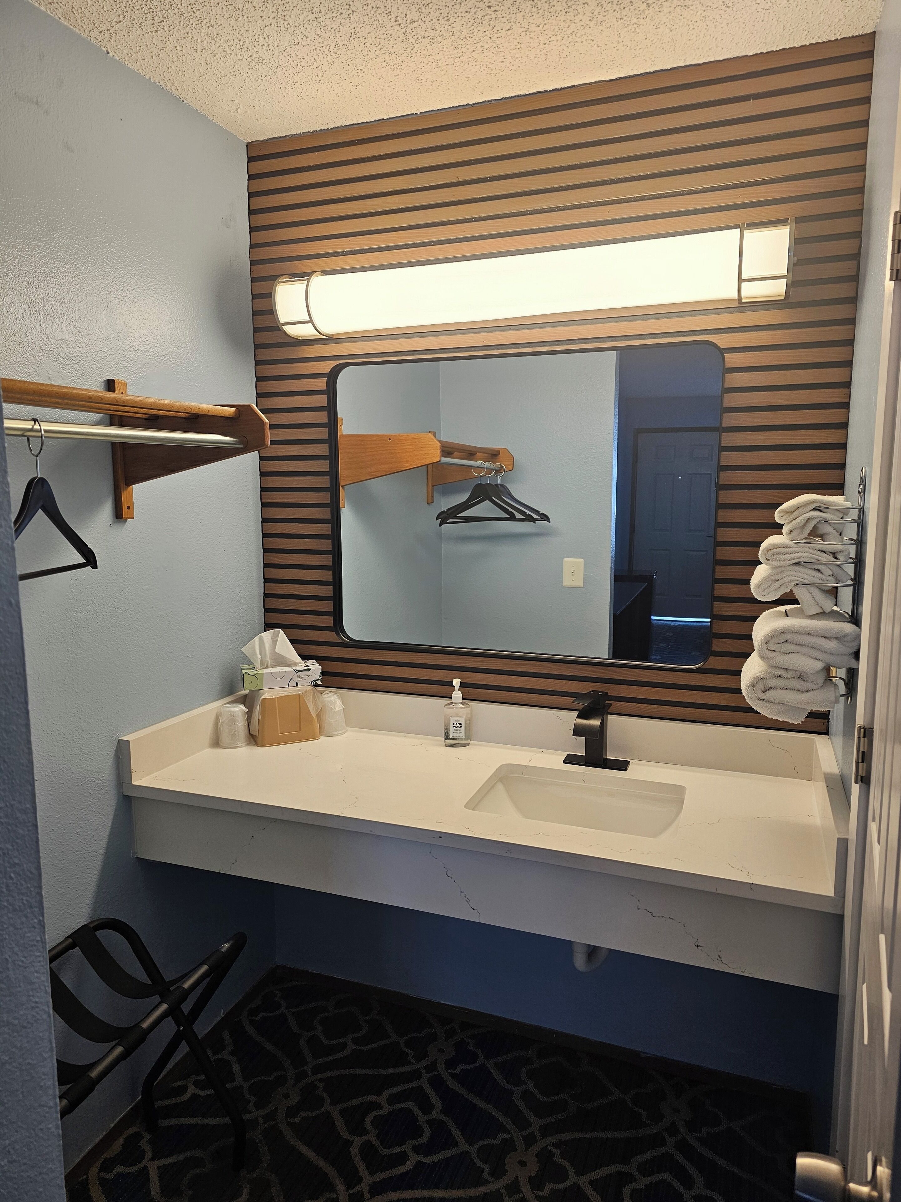 Un baño con pared de panel de madera, un espejo, un lavamanos con un perchero para toallas y un perchero para abrigos.