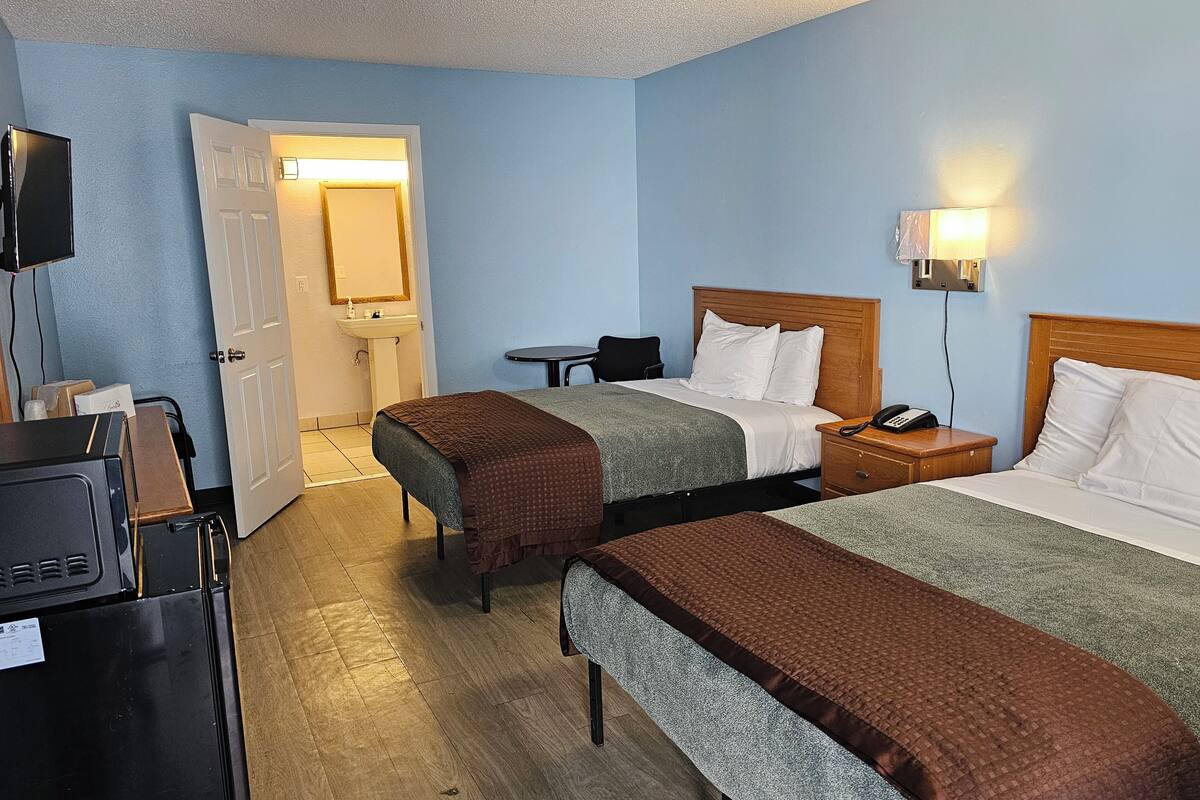 Une chambre d’hôtel avec deux lits, un bureau, une chaise, une télévision et une salle de bain visible à travers une porte ouverte.