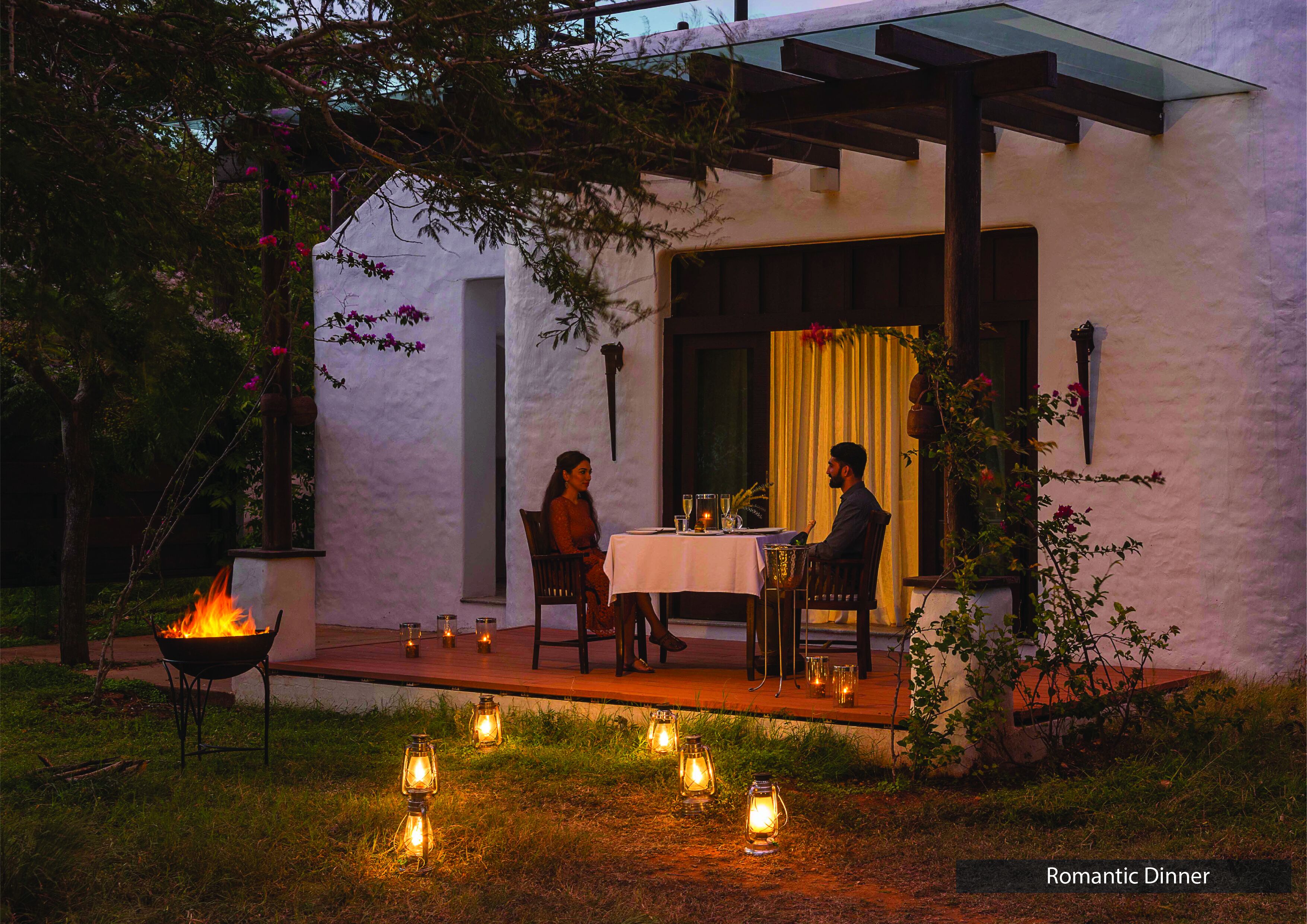 Cena romántica con una mesa y sillas frente a un edificio, rodeado de velas y fuego.