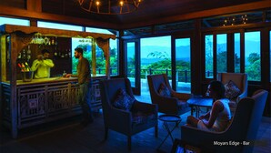 Un espace bar avec un barman, des sièges confortables et de grandes fenêtres offrant une vue sur le paysage.