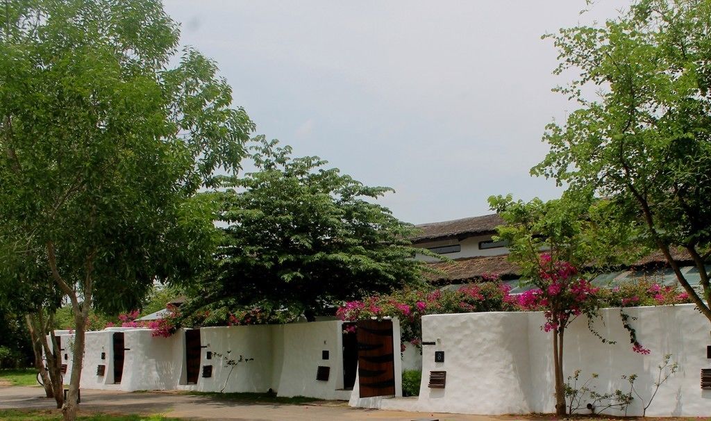 A traditional building with white walls and multiple doorways, surrounded by lush greenery and flowering plants.
