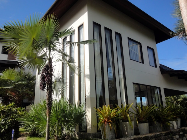 A modern two-story building with large windows and a well-maintained garden with various plants.