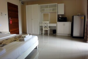 Una habitación de hotel con cama, escritorio, silla, armario y refrigerador.