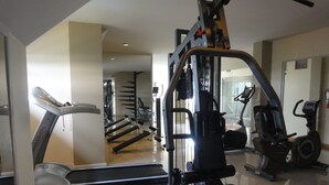 Un gimnasio con equipo de ejercicio, cinta de correr y un espejo que refleja el interior.