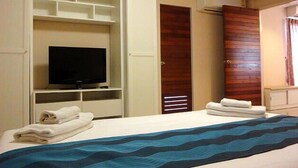 Una habitación de hotel con una cama, un televisor sobre un soporte, un armario y una puerta.