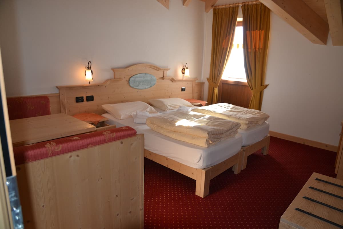 A wooden bed with two pillows and a blanket, a nightstand, and a wooden headboard with wall sconces.