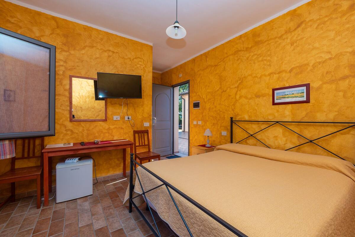 Een slaapkamer met een bed, een bureau, een stoel, een televisie en een kleine koelkast.