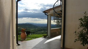 An open doorway leading to a balcony with a view of a green landscape and distant hills.