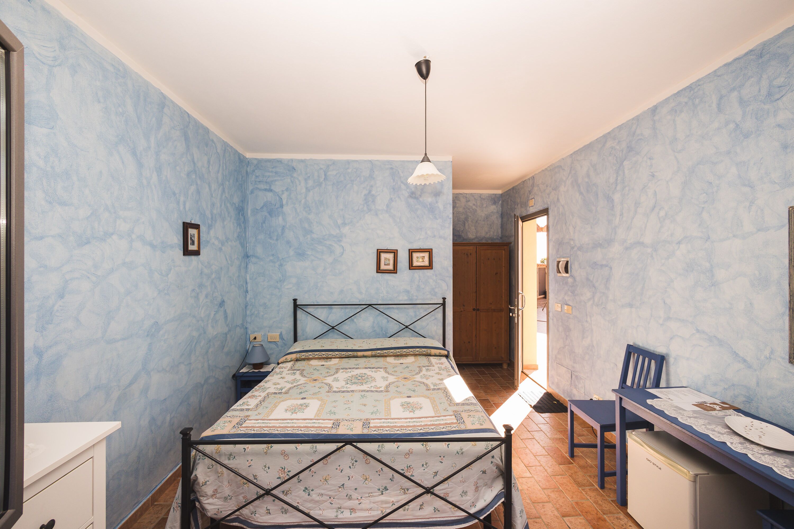 A bedroom with a bed, a desk, and a chair. There is a door leading to another room.
