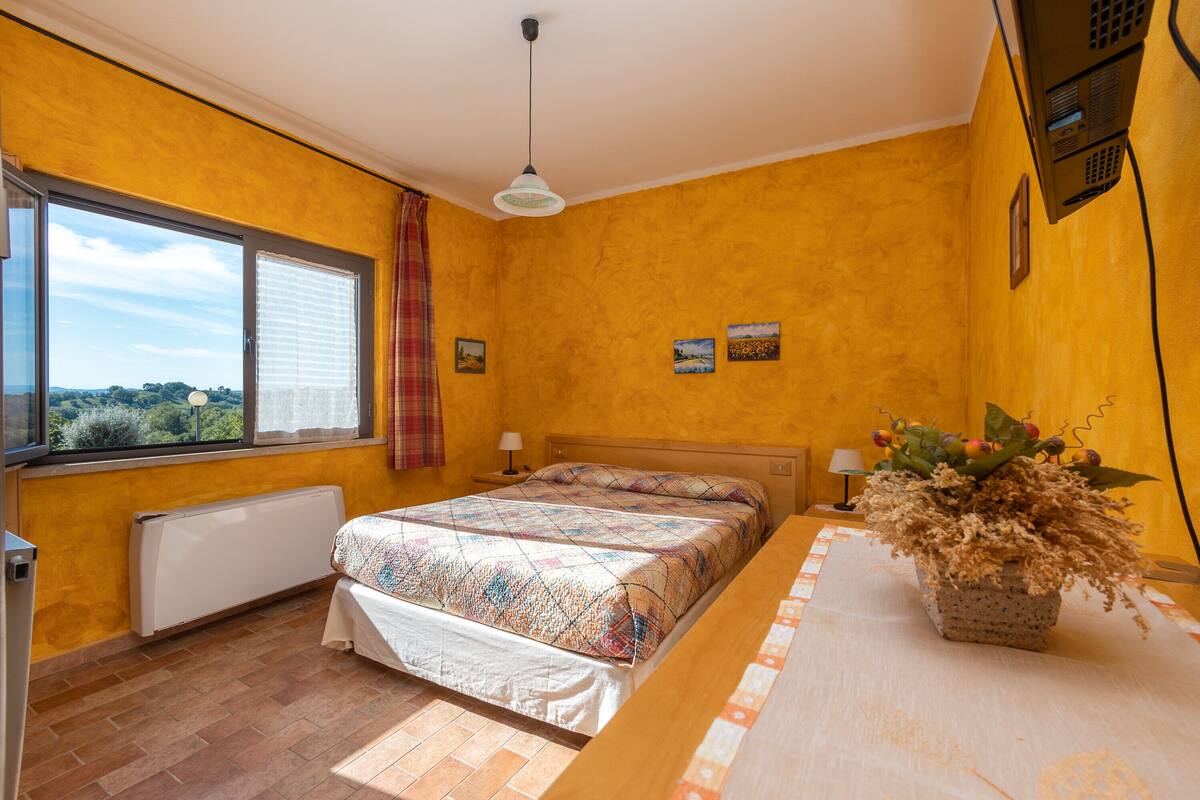 Een slaapkamer met een bed, een raam met uitzicht, een radiator en een tafel met een plant.