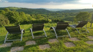 Three lounge chairs on a stone pathway with a scenic view of rolling hills and greenery.