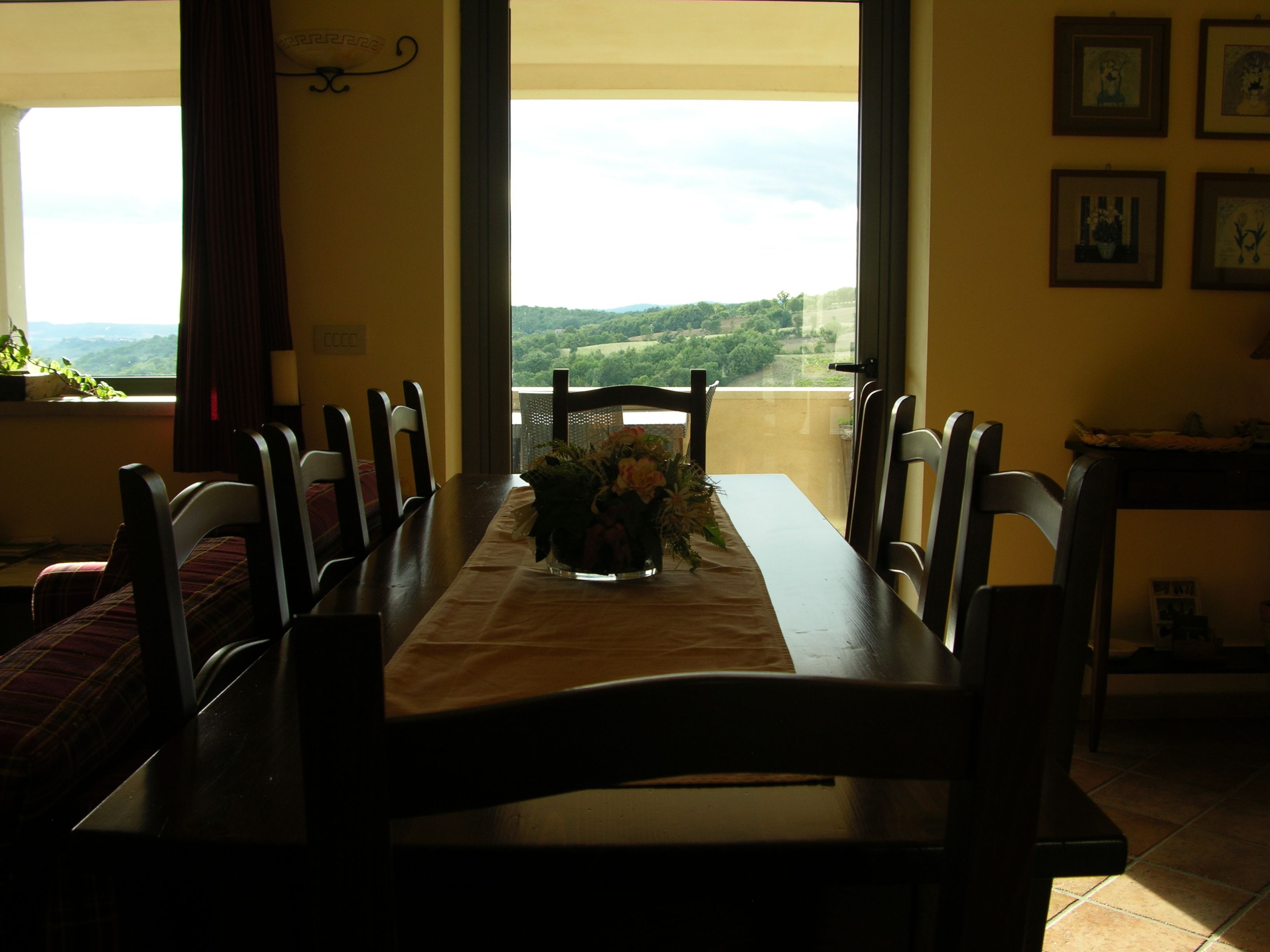 Un comedor con una mesa dispuesta para cuatro personas, sillas, un florero con flores y vistas a la vegetación a través de amplias ventanas.
