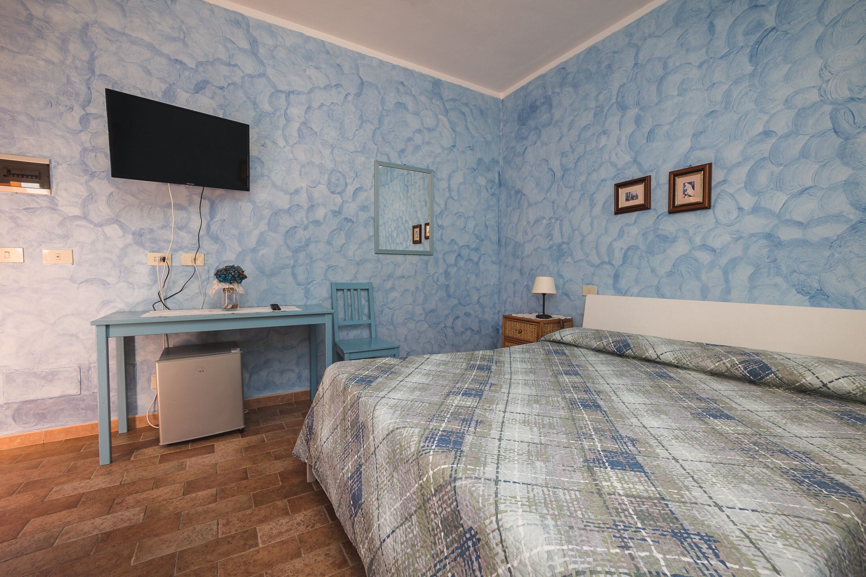 A bedroom with a bed, a desk, a television, and a mirror.