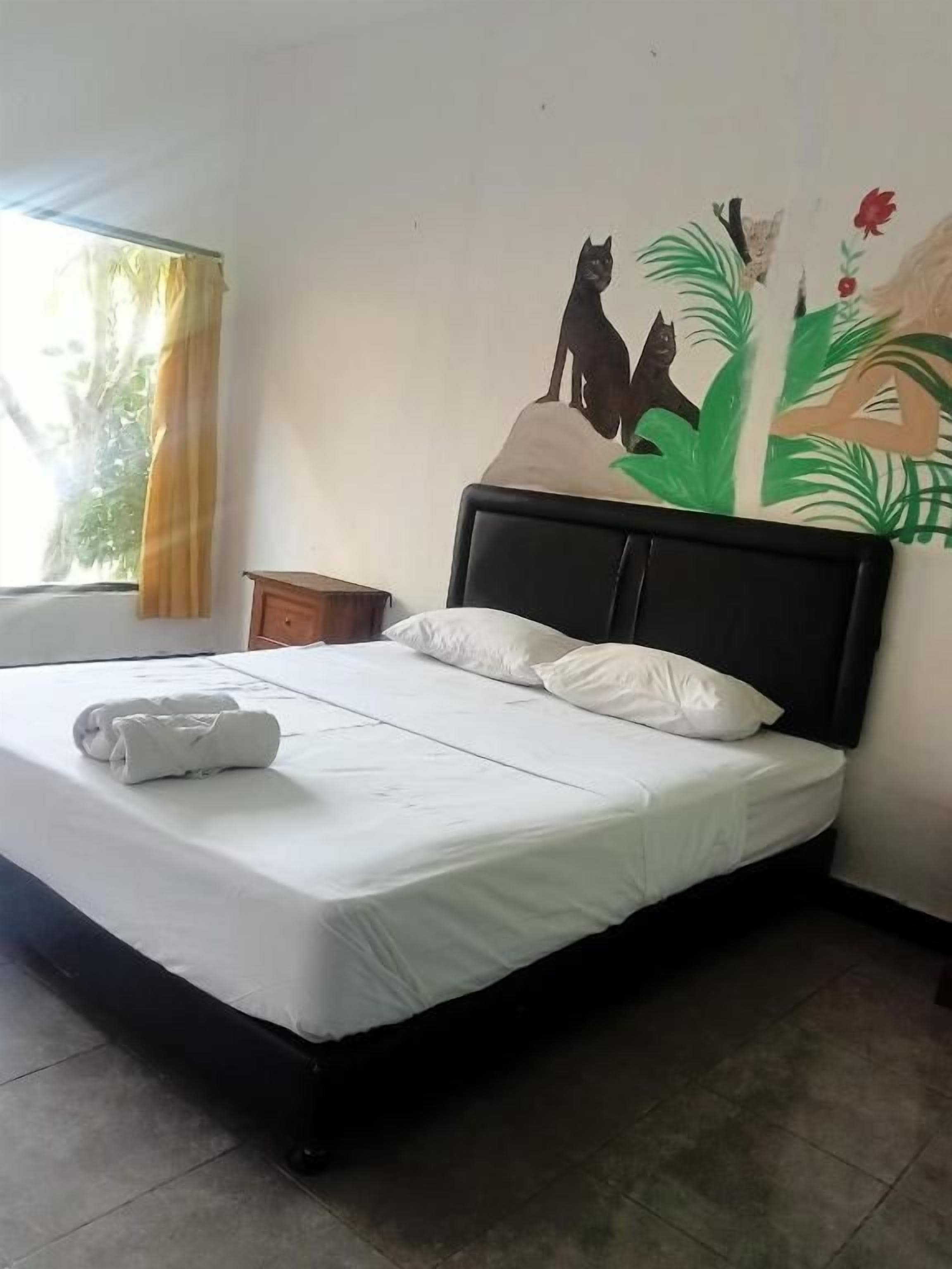 Una cama con ropa blanca, un cabecero negro y un mural en la pared con un gato y follaje.