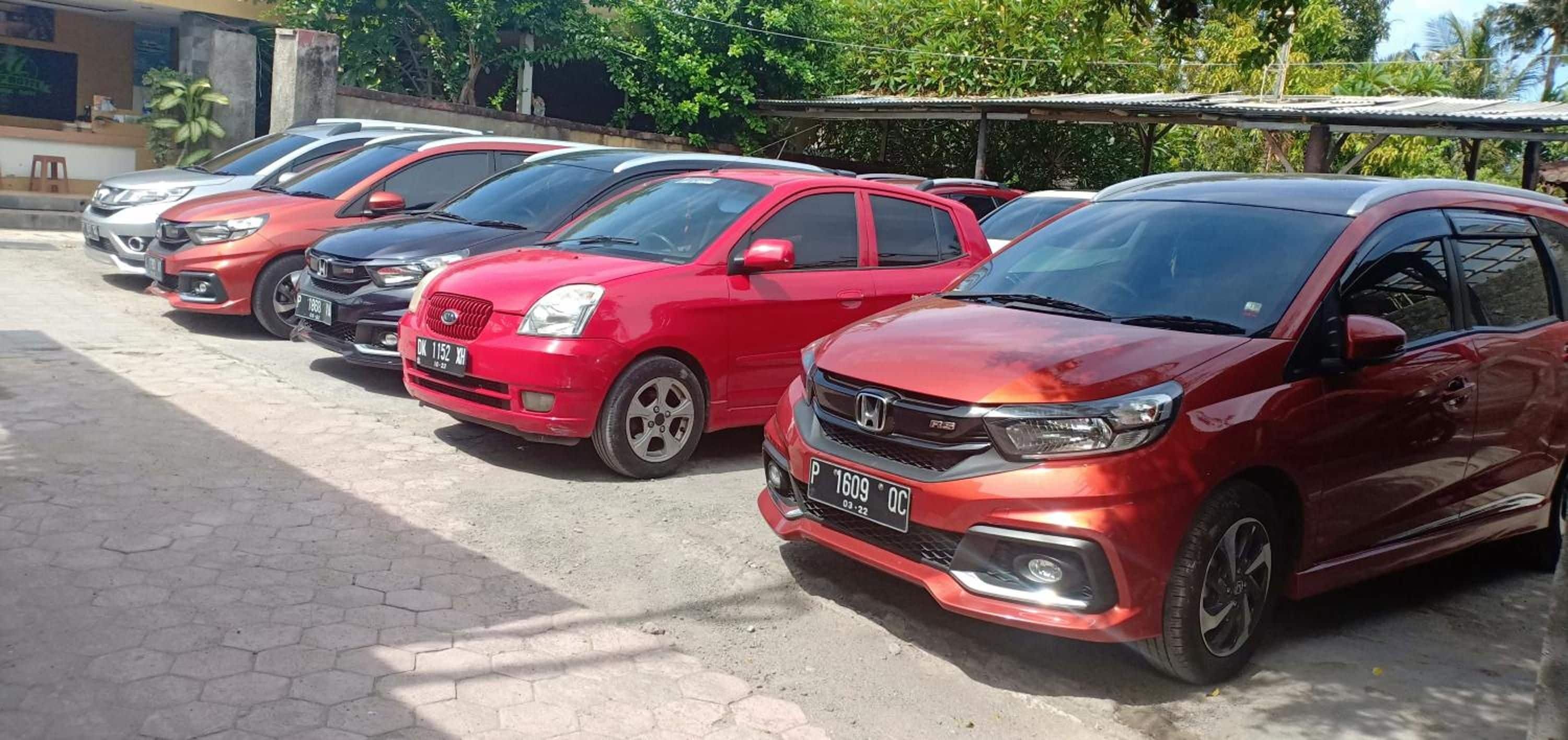 A row of parked cars, including a red Honda and a black Toyota, in a parking lot with a tiled floor and a building in the background.