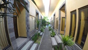 A corridor with a central pathway flanked by windows and plants, leading to a door at the end. - Vico Hotel (Nusa Dua)