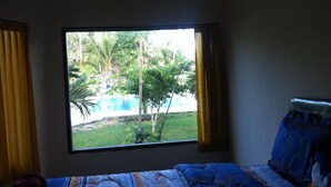 A bedroom with a large window, a bed with patterned bedding, and curtains. - Vico Hotel (Nusa Dua)