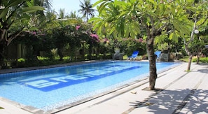 Una piscina con superficie de agua azul cristalina, rodeada de exuberante follaje y palmeras.