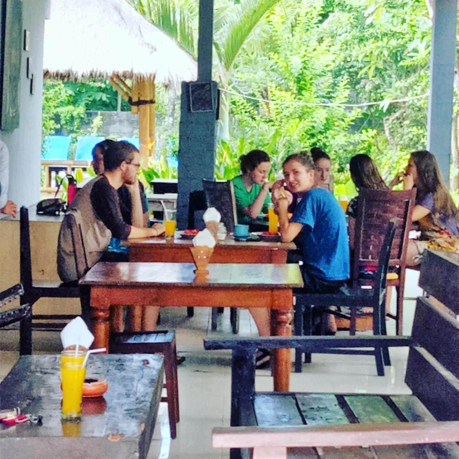 An outdoor dining area with wooden tables and chairs, surrounded by greenery.