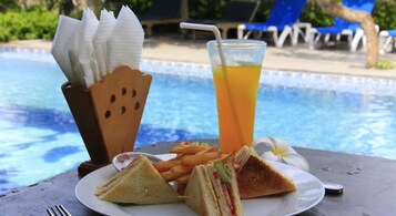 Una mesa con un plato de sándwiches, papas fritas y una bebida junto a una piscina.