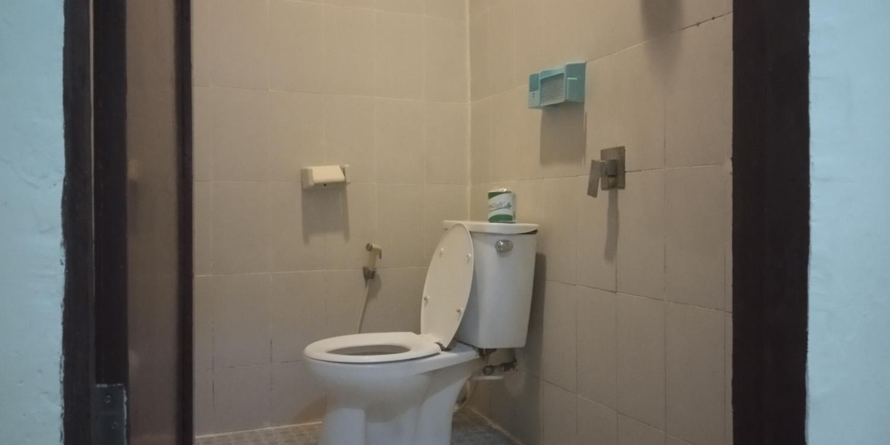 A small, enclosed bathroom with a toilet, a toilet paper holder, and a hand dryer.