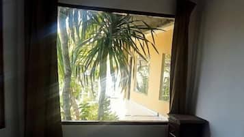 A hotel room with a bed, a window with curtains, and a view of palm trees.