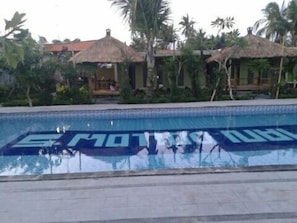 Una piscina en un entorno tropical, con palmeras y construcciones de techo de paja.