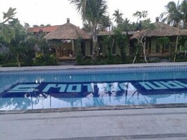 Una piscina en un entorno tropical, con palmeras y construcciones de techo de paja.