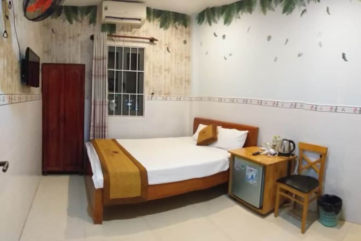 A bedroom with a bed, a wooden nightstand, a chair, a small cabinet, and a window with curtains.