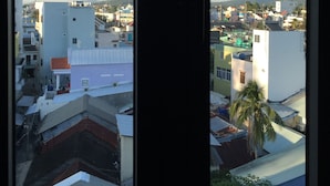 Une vue depuis une fenêtre donnant sur un paysage urbain avec différents bâtiments, dont un imposant bâtiment blanc surmonté d’un toit rouge.