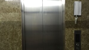 Une porte d’ascenseur en métal, avec un panneau de commande et un téléphone fixé au mur à côté.