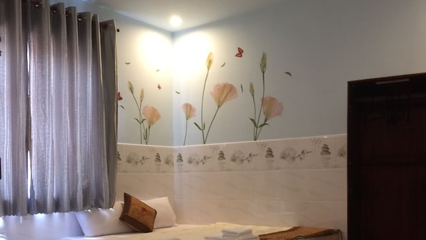 Une chambre d’hôtel avec un grand lit, une tête de lit en bois, une salle de bain avec douche et un mur recouvert d’un papier peint à motifs floraux.