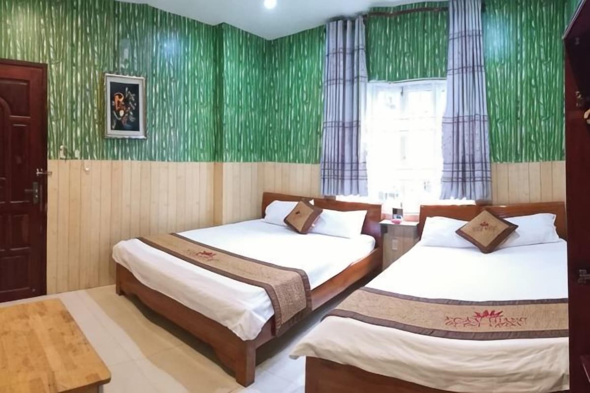 A room with two beds, a wooden bench, and a window with curtains.