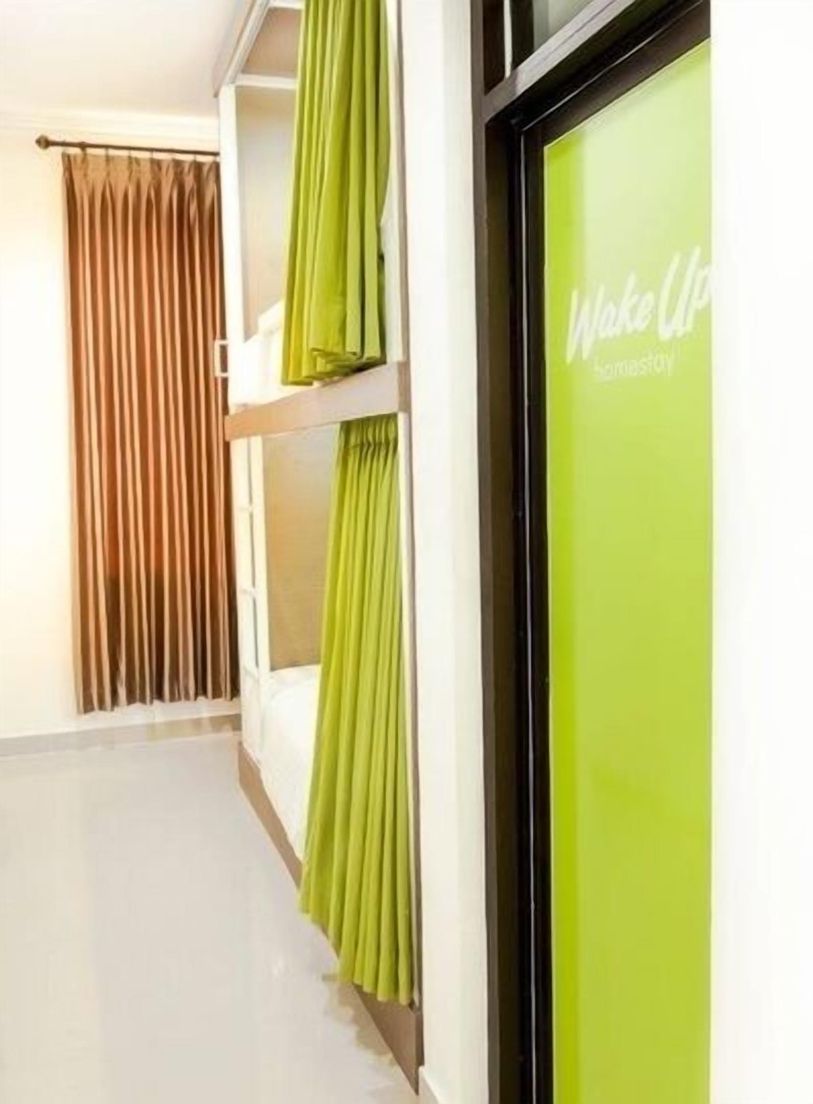 Un couloir d’hôtel avec un rideau vert, un mur blanc et une fenêtre également dotée d’un rideau.